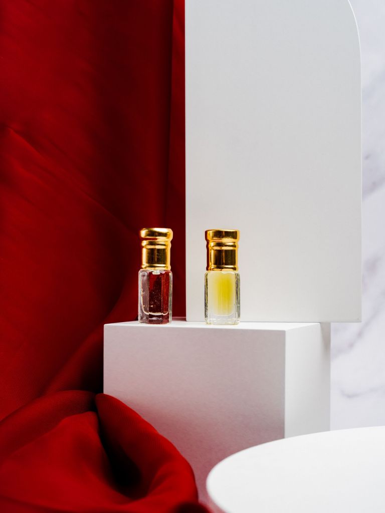Two perfume bottles on a white platform beside red fabric