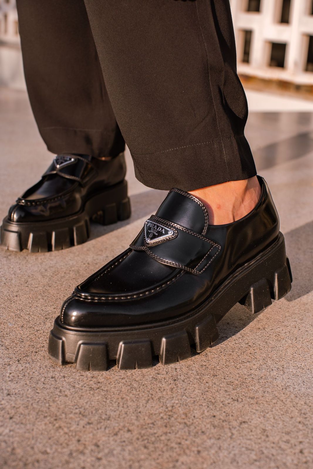 Black chunky-soled leather loafers worn with brown trousers.