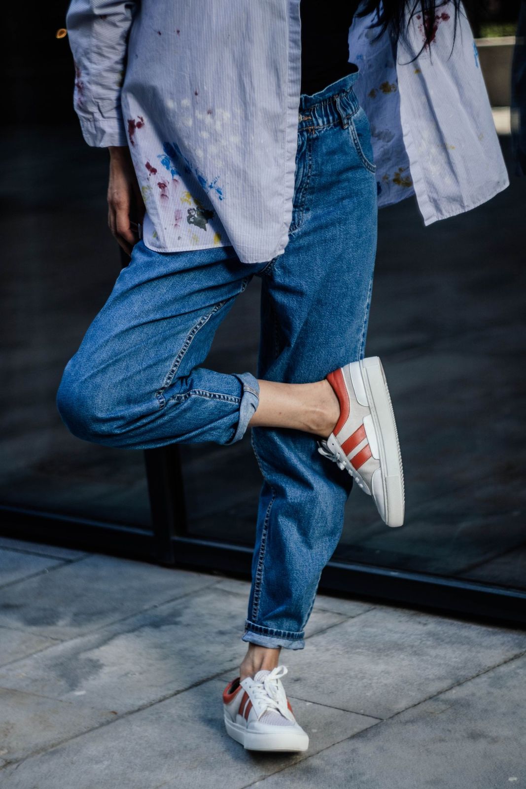 Striped low-profile sneakers worn with cuffed blue jeans and a loose shirt.